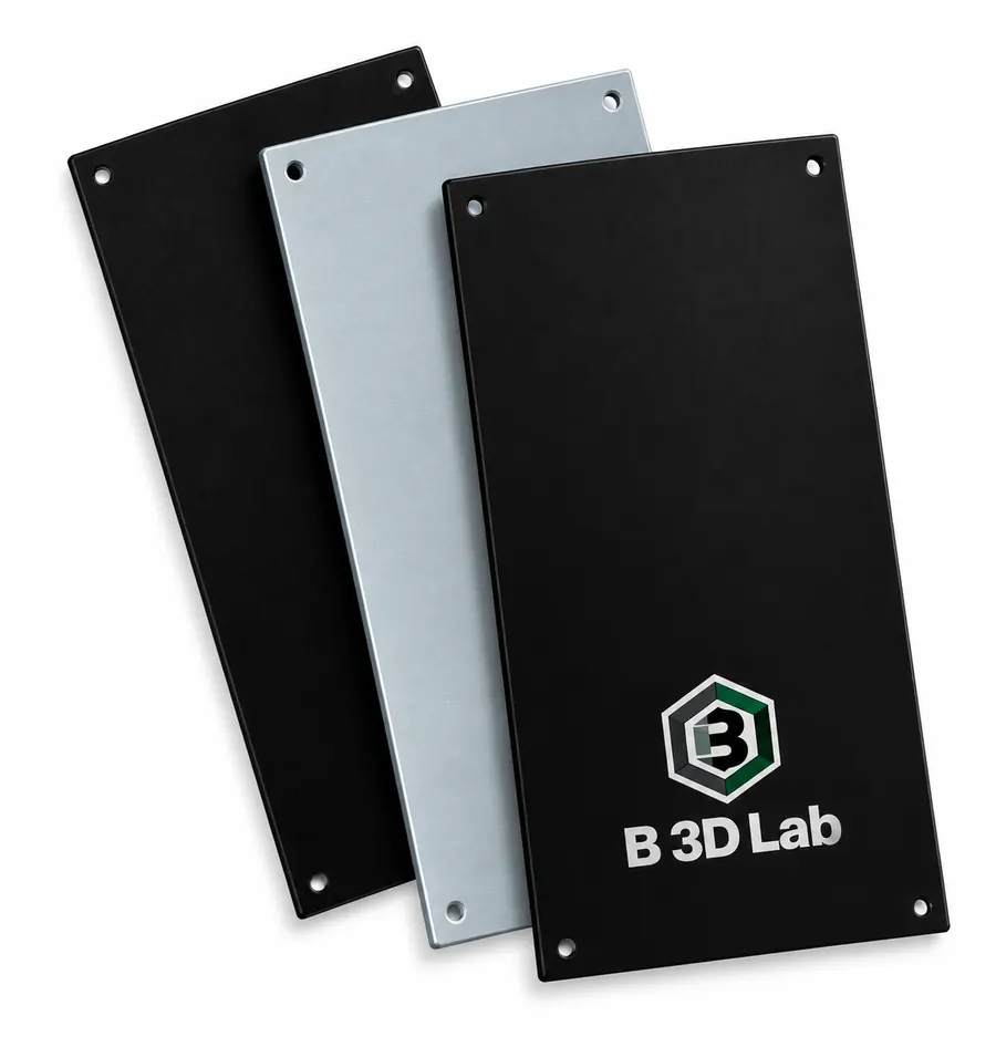 Tres clichés de tampografía superpuestos —dos de polímero negro y uno de acero pulido— con el logotipo de B3D Lab grabado en el frontal.