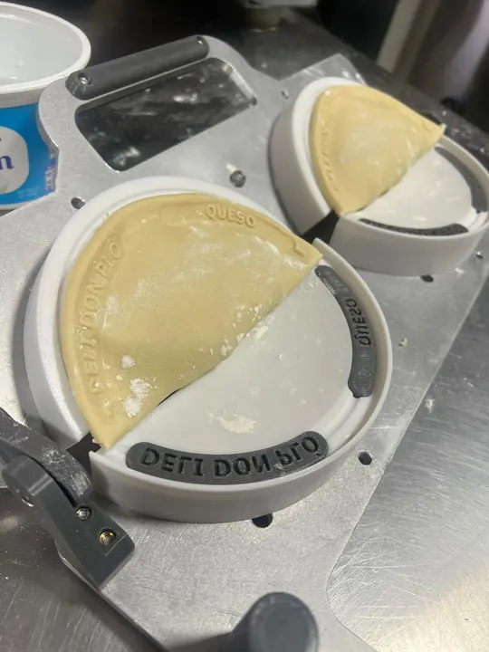 El molde en uso sobre la mesa de trabajo, marcando una empanada de masa.