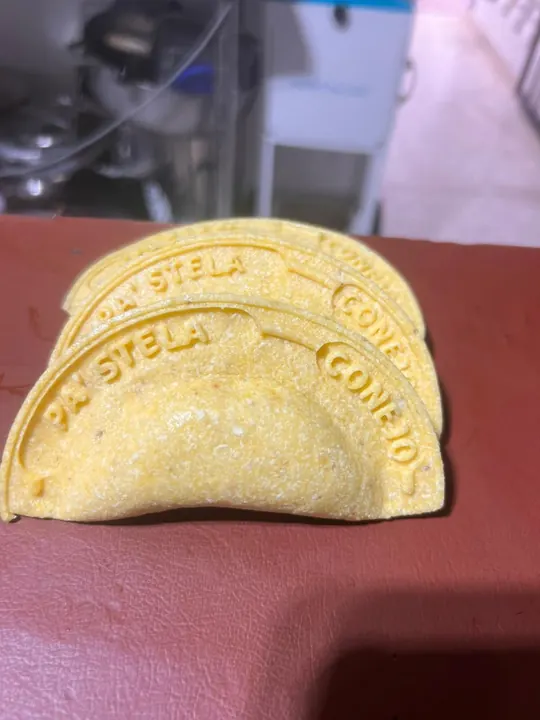 Dos empanadas de maíz con el nombre del negocio y el relleno grabados en relieve en el borde.